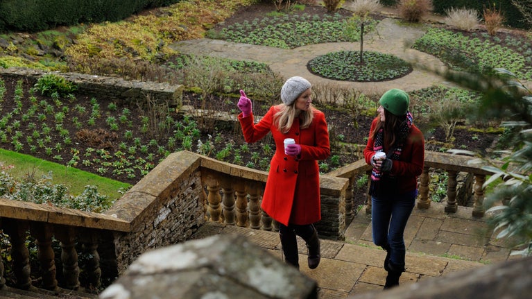 Two women in winter clothes chatting as they climb the stone steps in the gardens at Upton House, Warwickshire